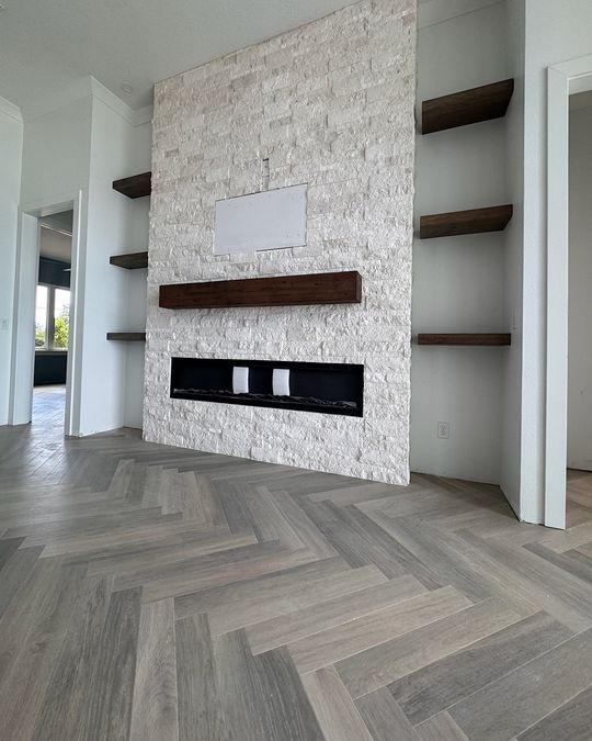 A stone fireplace wall with wood shelves over a gray herringbone floor.