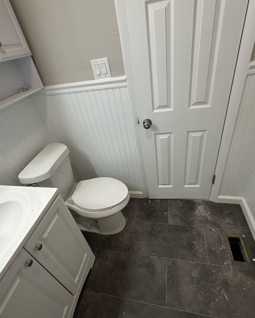 A bathroom with a large dark tile floor and white wainscoting.