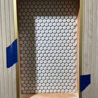 A shower niche with a round white mosaic and a gold trim edge.