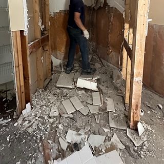 An old shower torn out down to the studs, with broken tile on the floor.