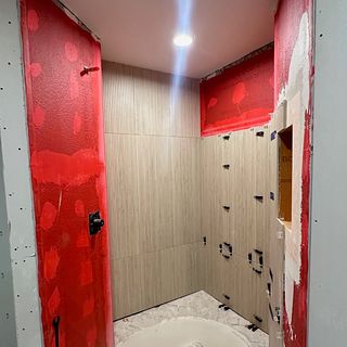 A red waterproofing membrane on the shower walls and floor, with wood-look tile going up.