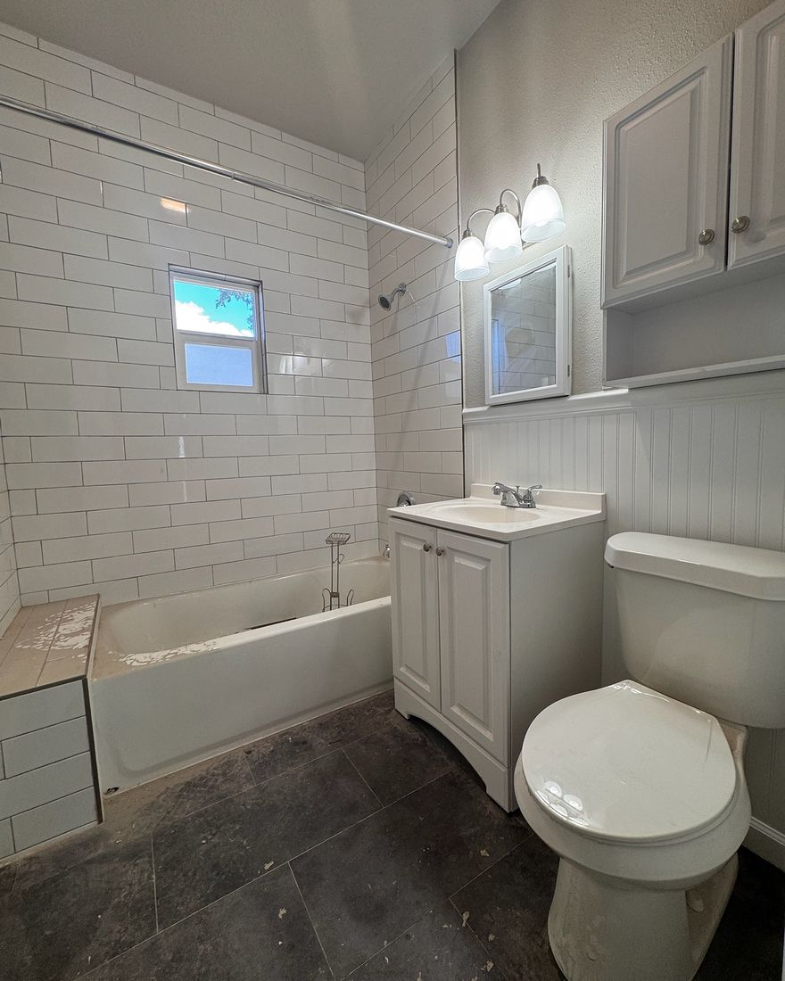 A guest bathroom with a subway tile tub surround, a vanity and a dark tile floor.