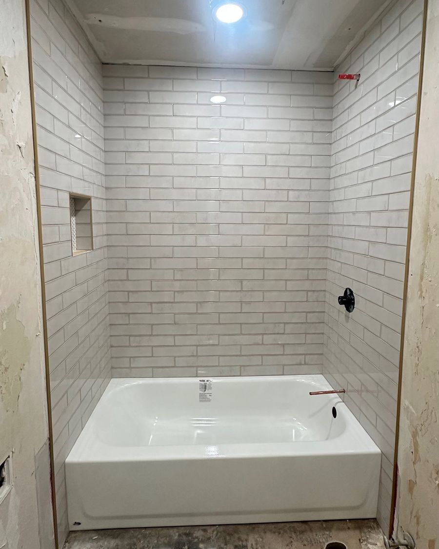 A bathroom halfway through: subway tile around a new tub and the floor still bare.