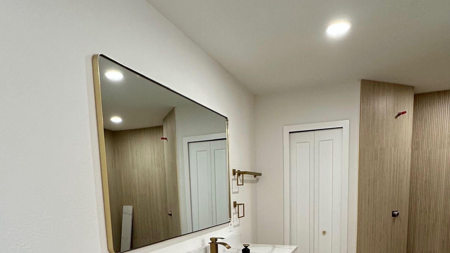 A bathroom with a white vanity, a stone top and a gold mirror.