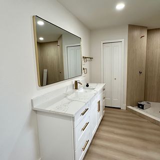 A white vanity with a stone top and a gold mirror over a new plank floor.