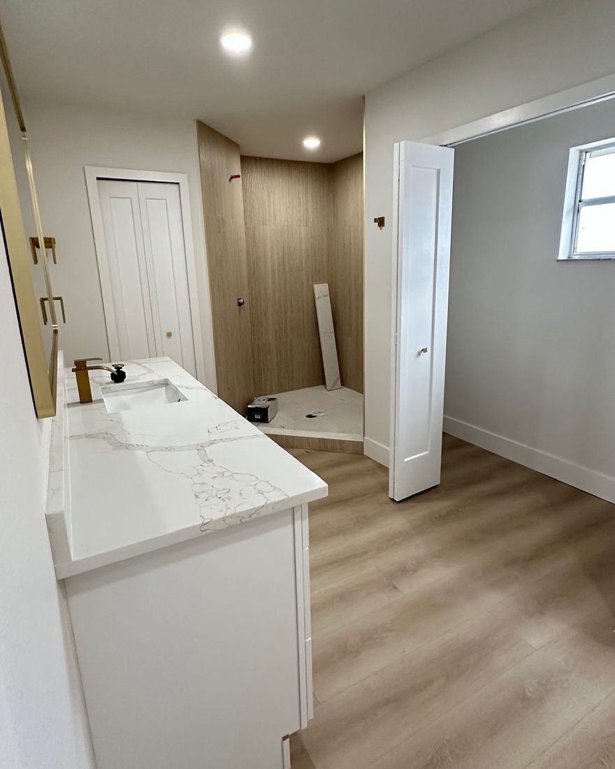 A bathroom with a stone-top vanity and a wood-look tile shower.