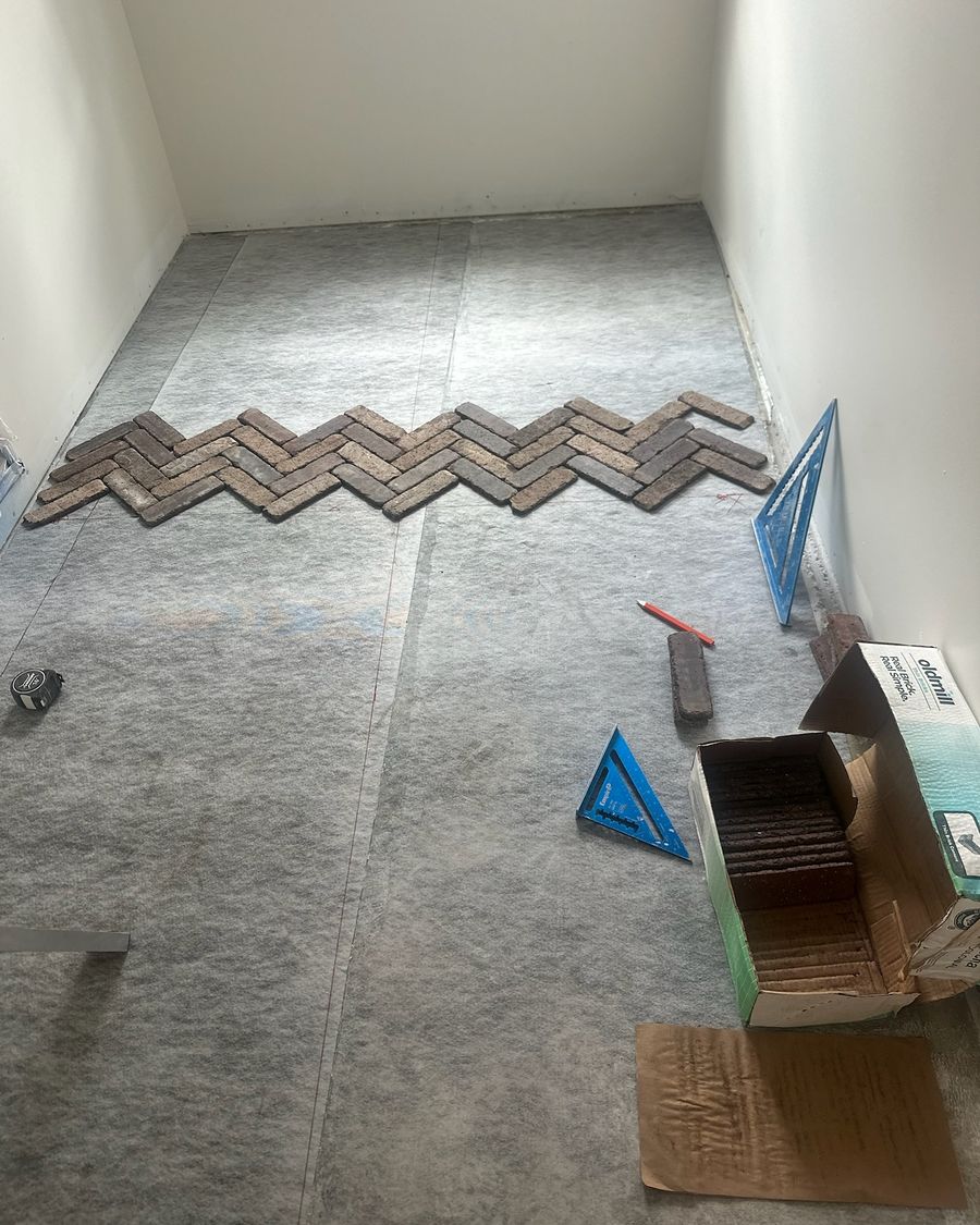 Bricks laid out dry in a herringbone row over a gray membrane.