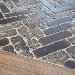 A herringbone brick floor meeting a wood floor in a straight line at a doorway.