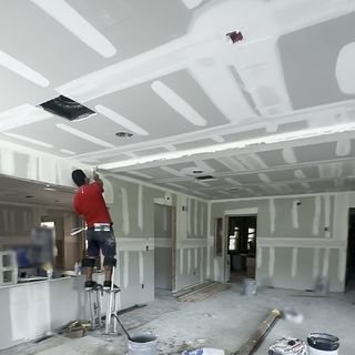 A finisher on stilts smoothing joint compound on a drywall ceiling.