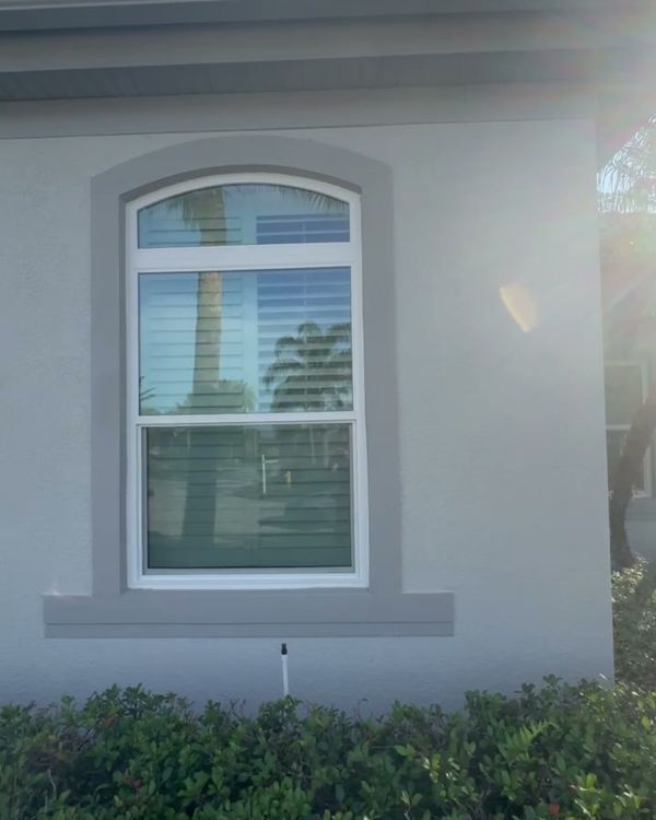 A stucco wall with fresh gray paint around an arched window, above a hedge.