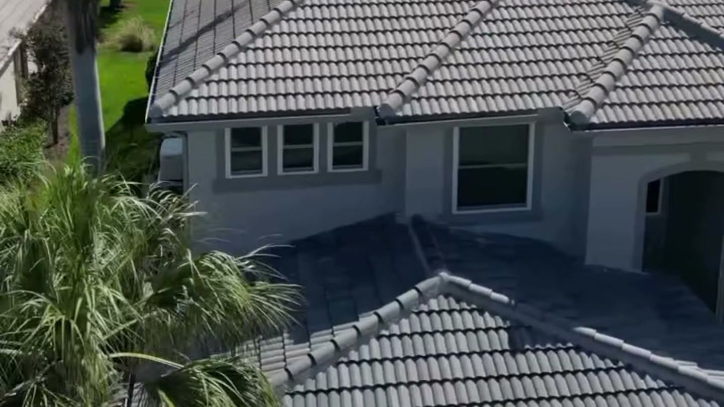 A repainted gray stucco home with palm trees and the water behind it.