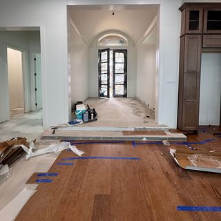 Wide hardwood planks going down over a concrete slab, with blue tape on the fresh rows.