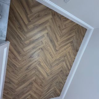 A herringbone plank floor with a white baseboard along its edge.