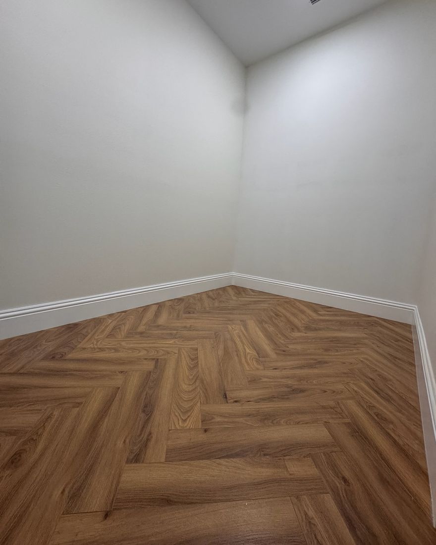 An empty closet with a wood-look herringbone floor and white baseboards.