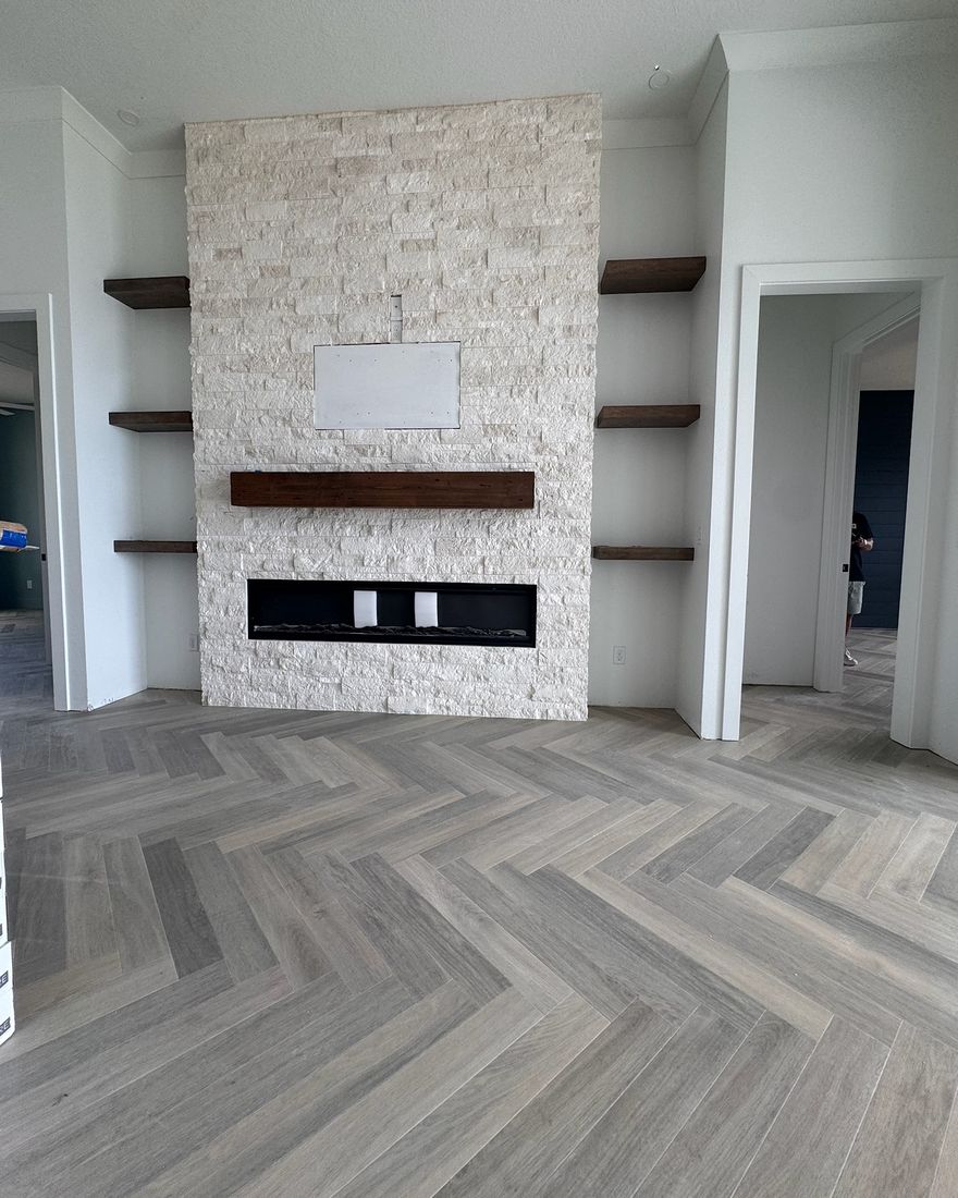 A stone fireplace wall with wood shelves over a gray herringbone floor.