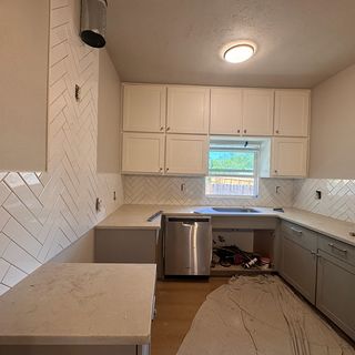 A white herringbone backsplash finished behind the range, with the floor protected.