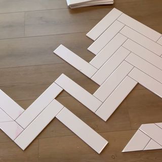 White tile laid out in a herringbone pattern on the floor before going on the wall.