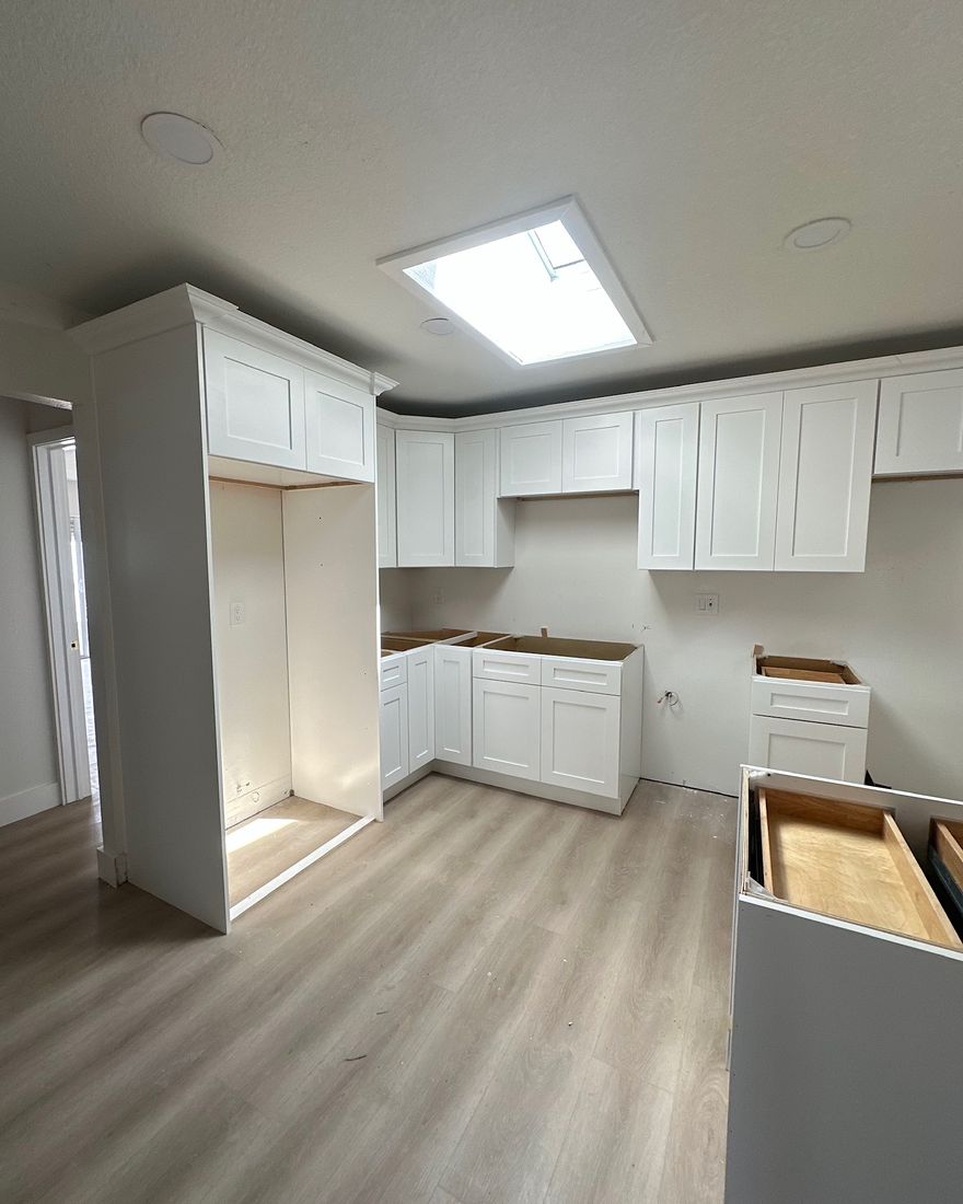 New white kitchen cabinets in place before the countertops, over a light plank floor.
