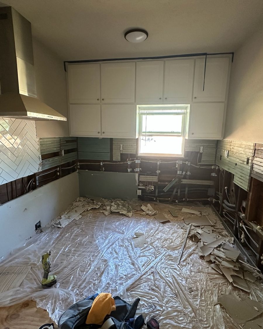 A kitchen on day one: the old lower cabinets and backsplash torn out, plastic over the floor.