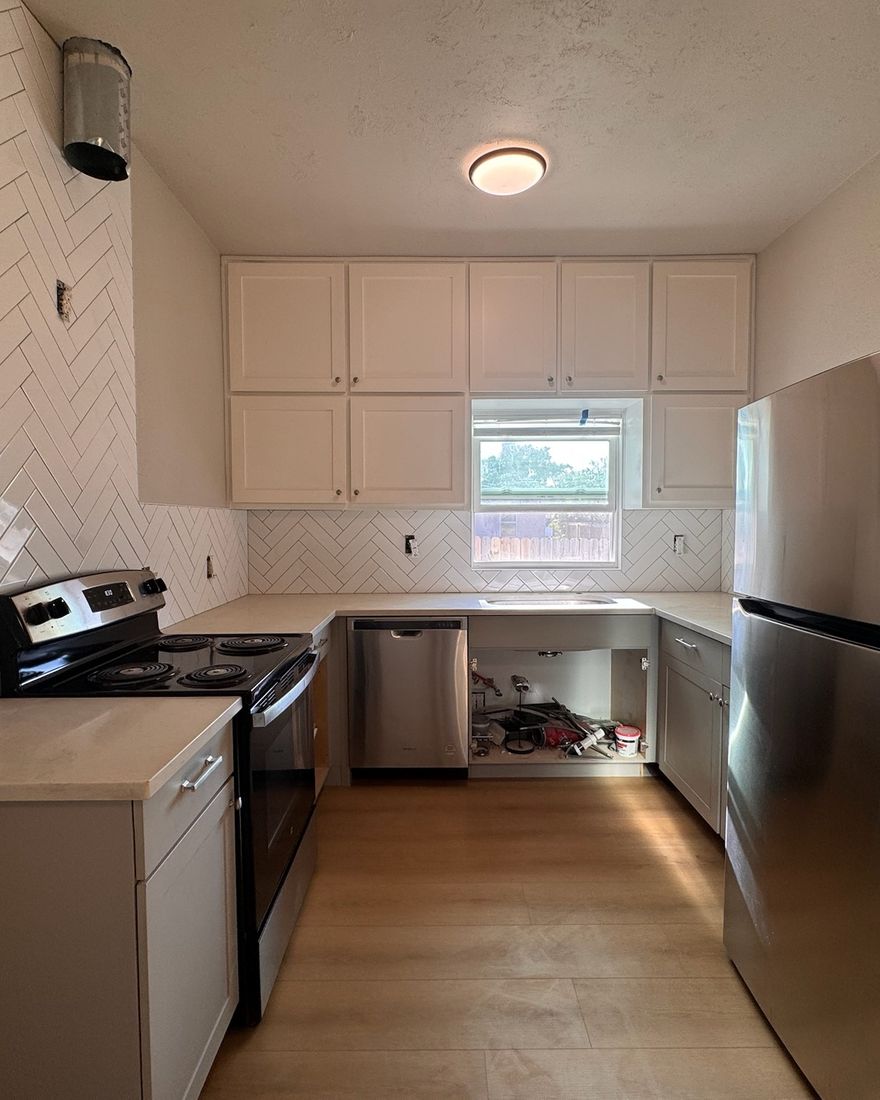 A kitchen in daylight with a white herringbone backsplash and a wood-look plank floor.