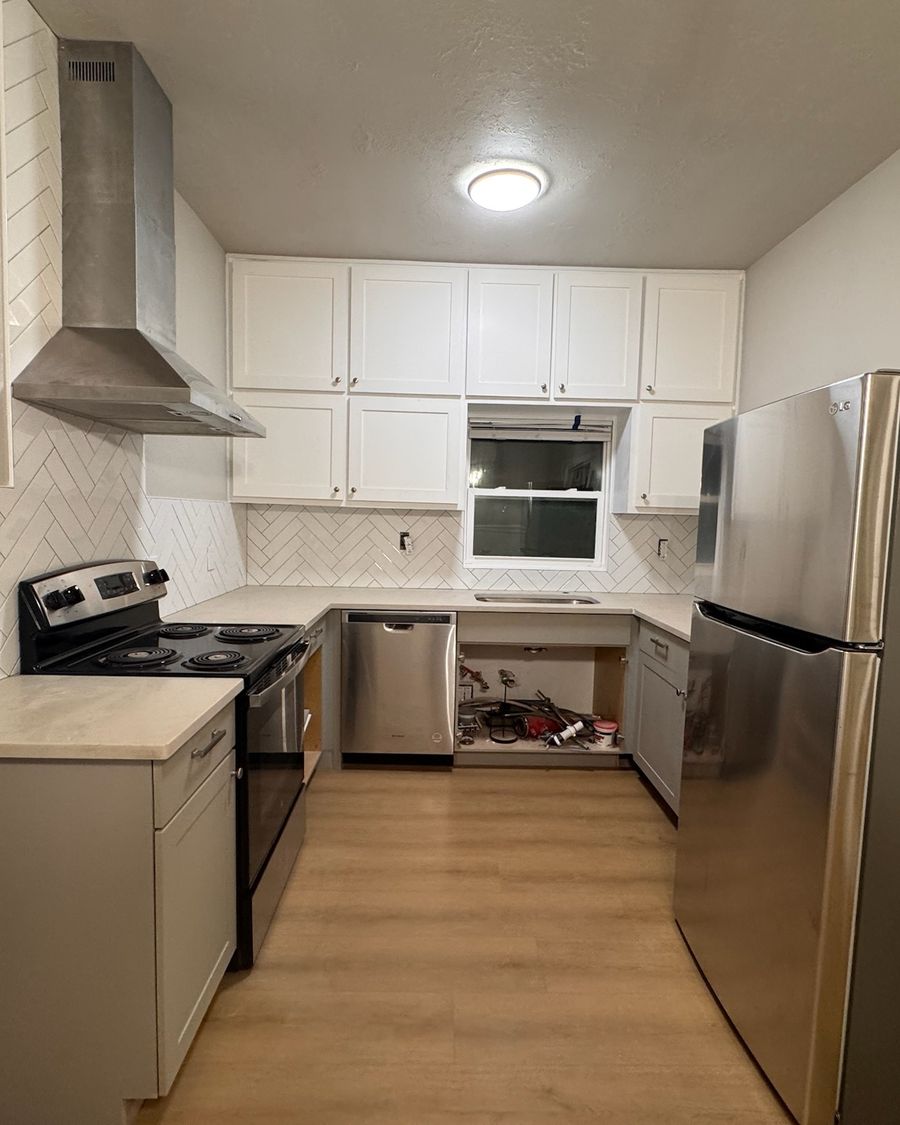The same kitchen when done: white cabinets, a herringbone backsplash and a new plank floor.