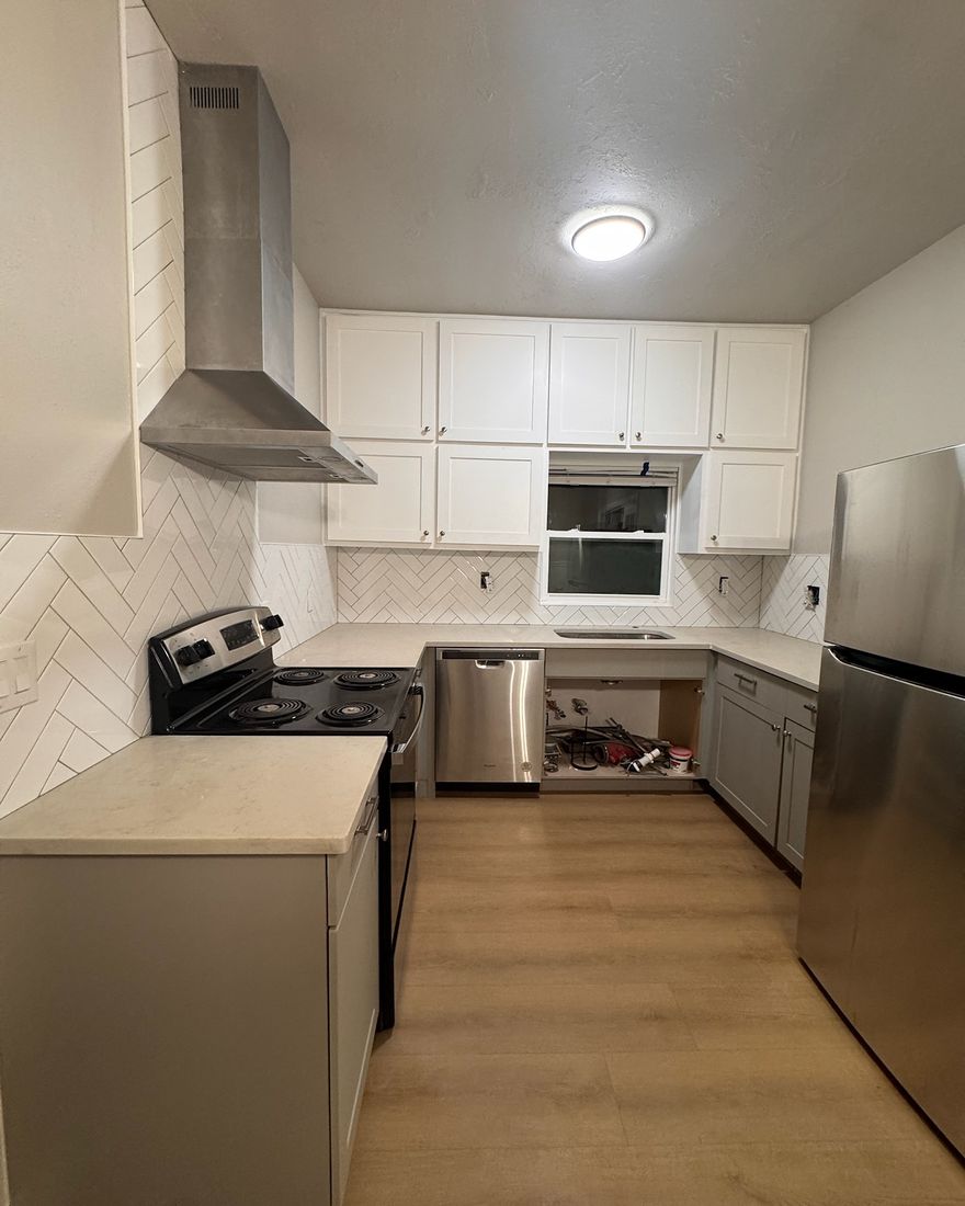 A U-shaped kitchen with white cabinets, a herringbone backsplash and a plank floor.