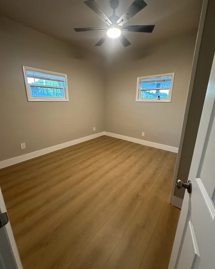 A freshly painted bedroom with white baseboards and a new floor.