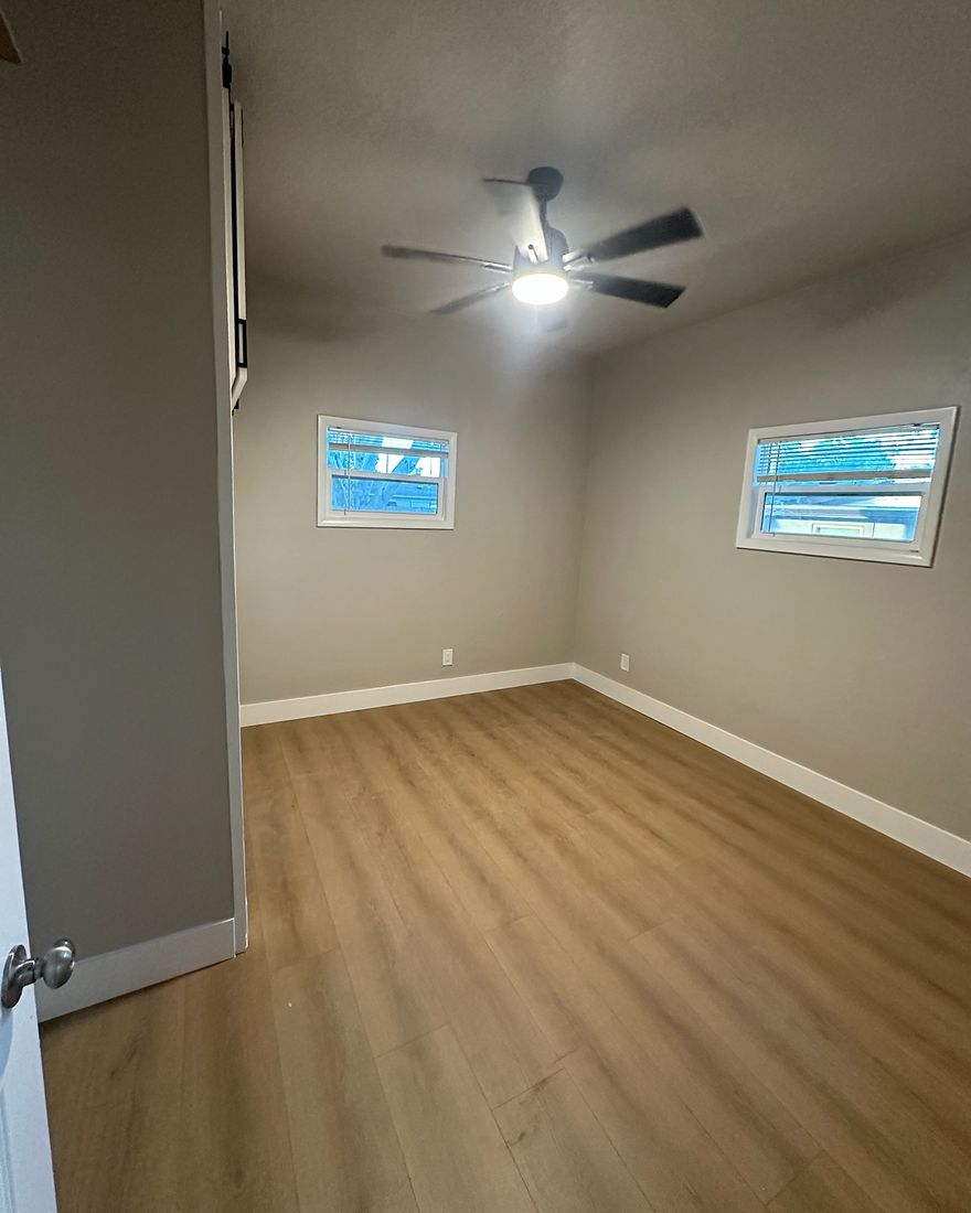 An empty bedroom with a wood-look plank floor, white baseboards and two windows.