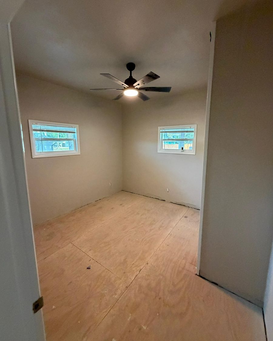 A bedroom on day one: new subfloor sheets, a ceiling fan and two windows.