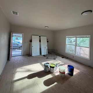 Paint cans on a bare subfloor in a freshly painted living room.