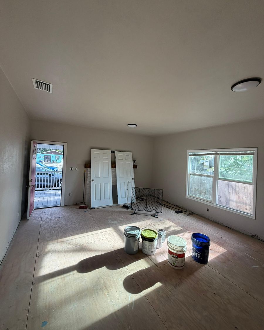 A living room with fresh paint on the walls and paint cans on the bare subfloor.