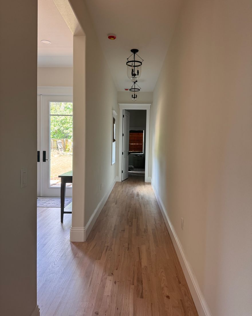 A long hallway with a natural hardwood floor and white baseboards.