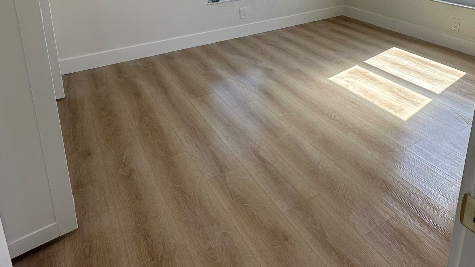 A bedroom with sunlight across a light wood-look plank floor.
