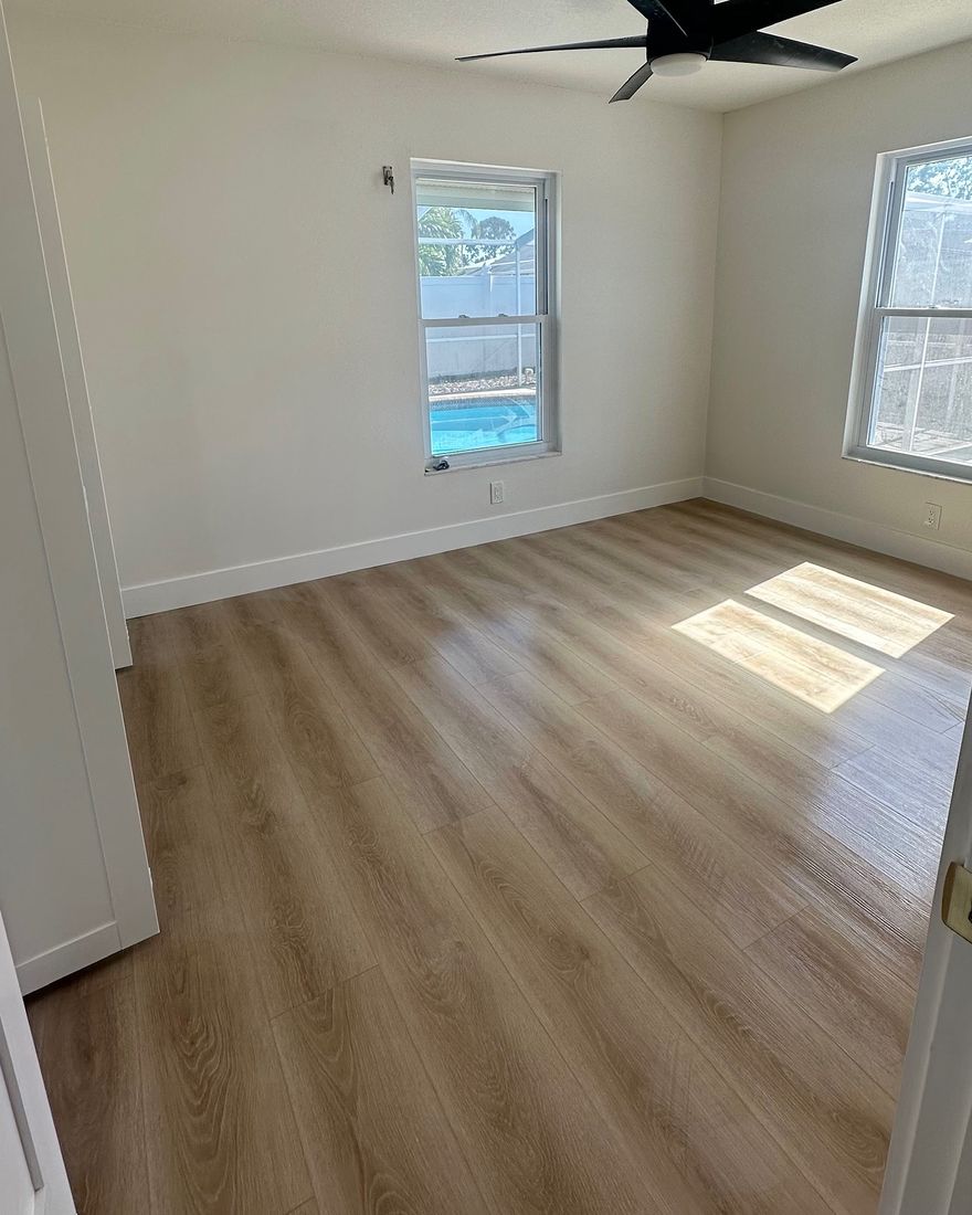 A bright bedroom with a light wood-look plank floor and white baseboards.