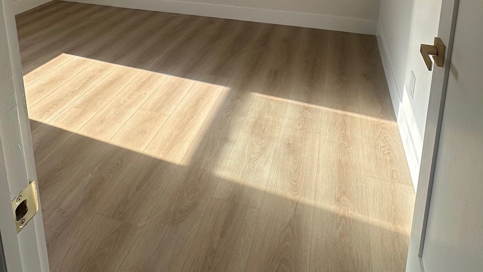A bedroom with white baseboards along a light wood-look plank floor.