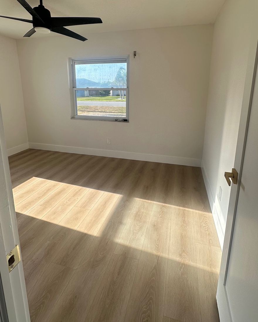 A bedroom with patches of sun on a light wood-look plank floor.