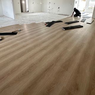 An open room with half of a new wood-look plank floor installed.