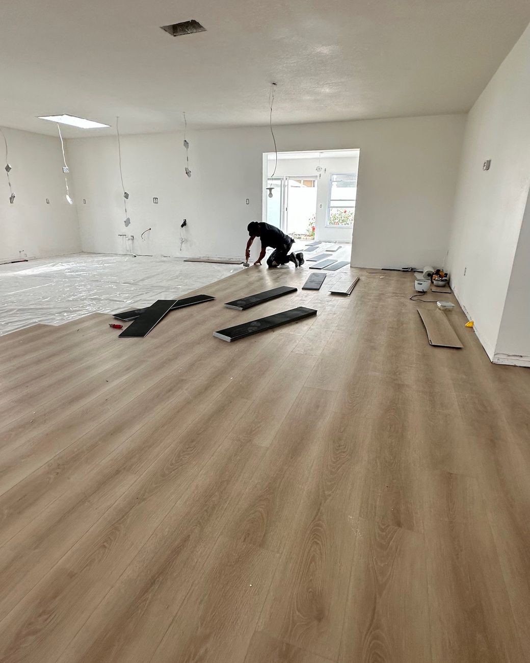 An installer kneeling to fit new wood-look plank flooring in a large open room.