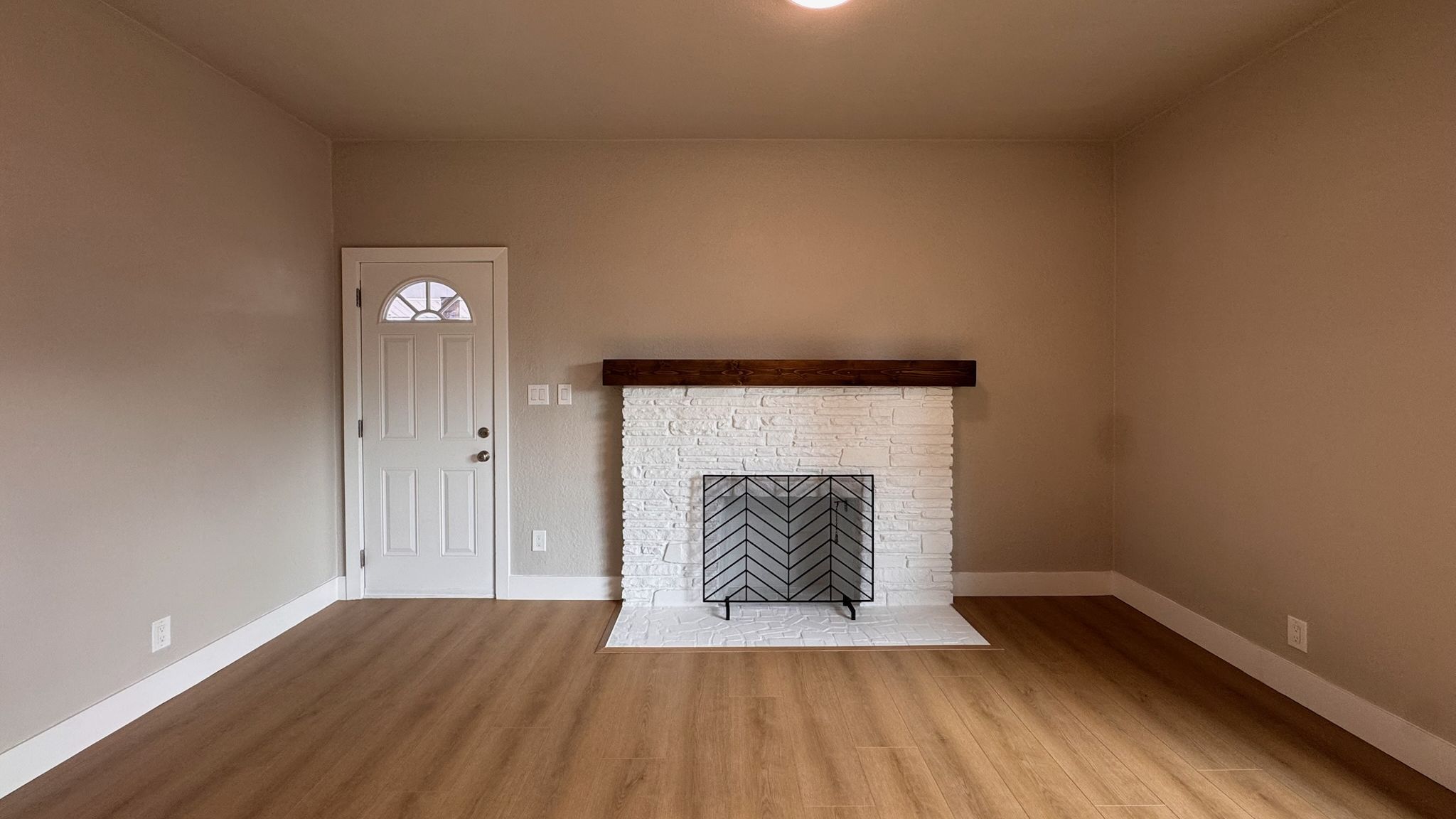 A living room with a white brick fireplace and a new wood-look plank floor in the sun.