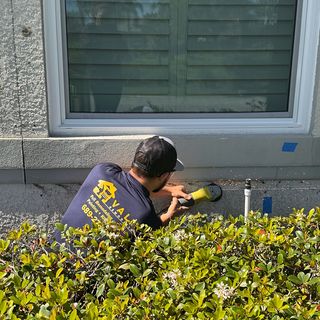 A painter in a Valin Remodeling shirt sanding the stucco under a window.