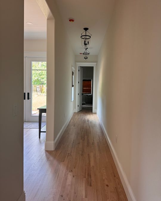 A long hallway with a natural oak hardwood floor and white baseboards.