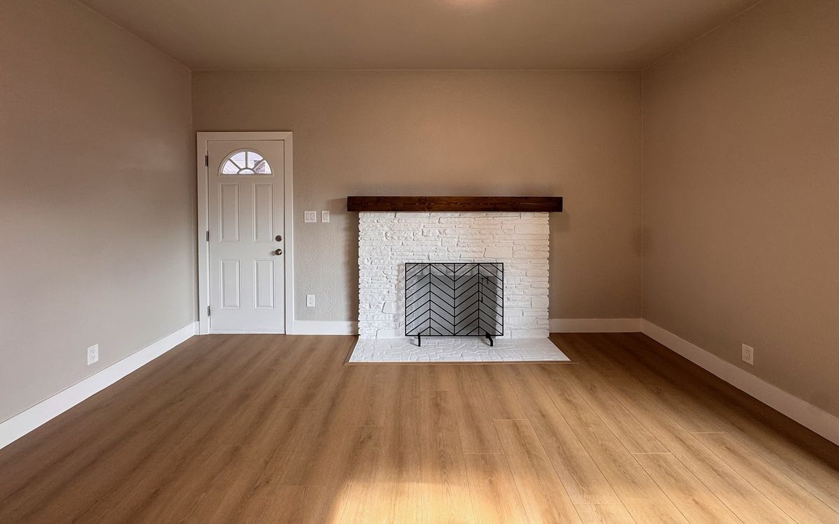 A living room with a white brick fireplace and a new wood-look plank floor in the sun.